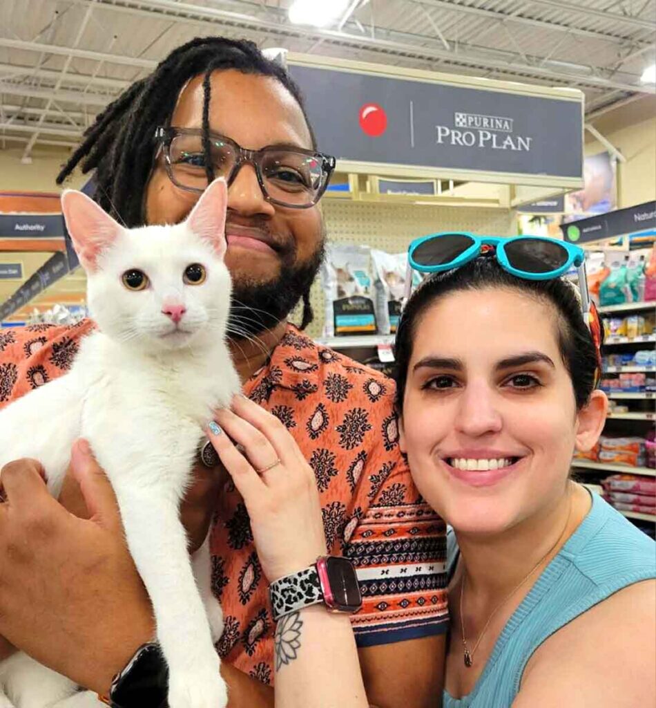 A man and woman holding a white cat at a pet supply store.