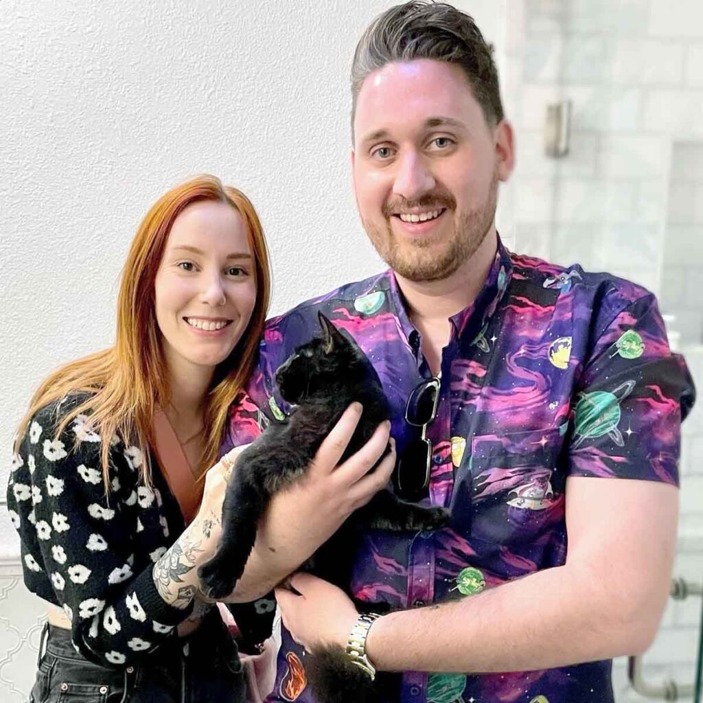 A man and woman holding a black cat.